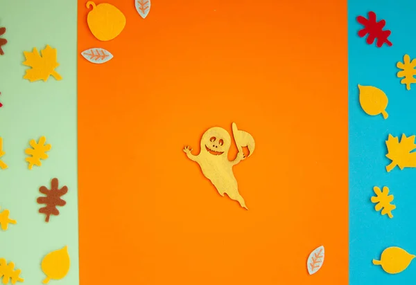 Paper leaves and ghosts for Halloween party are laid out on an orange background.