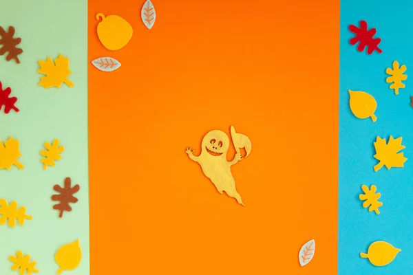 Paper leaves and ghosts for Halloween party are laid out on an orange background.
