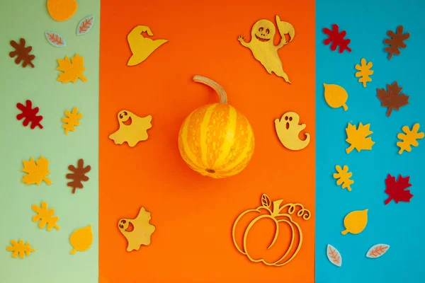 Paper leaves and ghosts for Halloween party are laid out on an orange background.