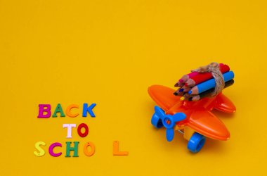 Sarı arka planda küçük bir oyuncak turuncu uçakta renkli kalemler..