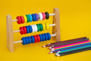 Çocuk okulu abaküsü ve sarı arka planda renkli tahta kalemler..