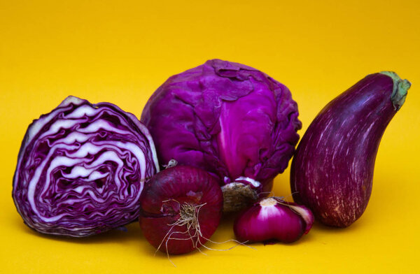 Vegetables - red cabbage, eggplant and purple onions - on a yellow background