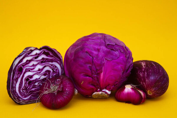 Vegetables - red cabbage, eggplant and purple onions - on a yellow background