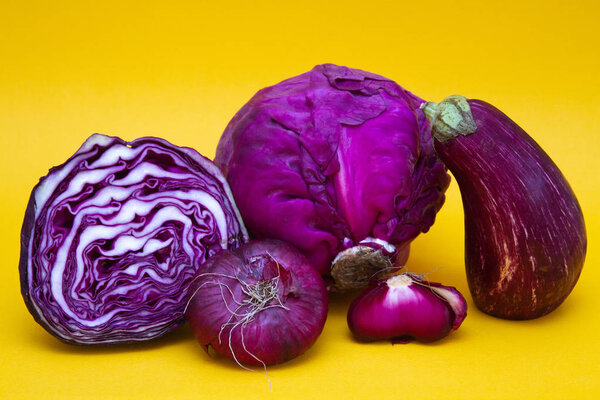 Vegetables - red cabbage, eggplant and purple onions - on a yellow background