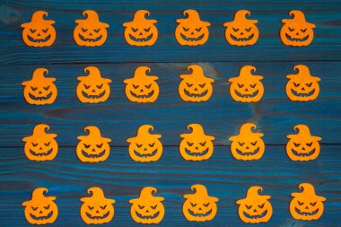 Ahşap mavi arka planda balkabağı yüzlü turuncu siluetler. Cadılar Bayramı için kompozisyon