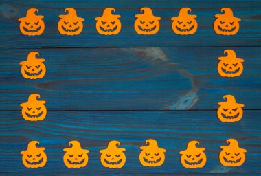 Ahşap mavi arka planda balkabağı yüzlü turuncu siluetler. Cadılar Bayramı için kompozisyon