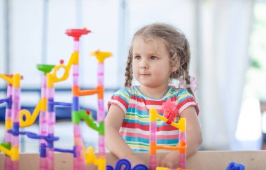 Küçük tatlı bir kız plastik bir inşaatçıyla oynar, bir çocuk küçük parçalardan bir kule inşa eder, bir masa oyunu, çocukların boş vakitleri.