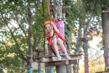Turuncu kasklı ve özel korumalı küçük bir kız, bir halat parkında, çocuk parkında, bir lunaparkta, bir eğlence parkında,.