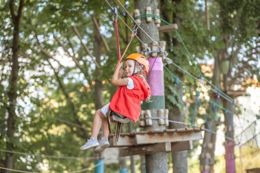 Turuncu kasklı ve özel korumalı küçük bir kız, bir halat parkında, çocuk parkında, bir lunaparkta, bir eğlence parkında,.