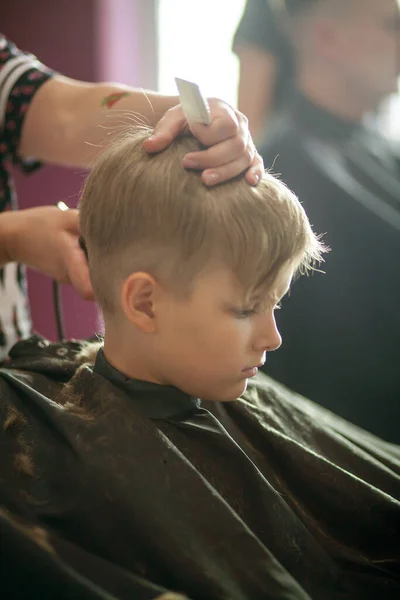 小さなかわいい男の子がスタイリストの美容室に座っています 子供は美容室で髪を切っています 理容室で子供 短い男性の散髪 — ストック写真
