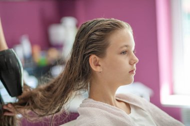 Güzel Avrupalı genç bir kız güzellik salonunda oturuyor, profesyonel kuaför stilisti uzun saçlı bir kızla çalışıyor..