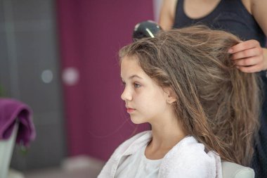 Güzel Avrupalı genç bir kız güzellik salonunda oturuyor, profesyonel kuaför stilisti uzun saçlı bir kızla çalışıyor..