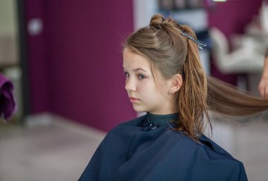 Güzel Avrupalı genç bir kız güzellik salonunda oturuyor, profesyonel kuaför stilisti uzun saçlı bir kızla çalışıyor..