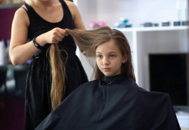 Güzel Avrupalı genç bir kız güzellik salonunda oturuyor, profesyonel kuaför stilisti uzun saçlı bir kızla çalışıyor..