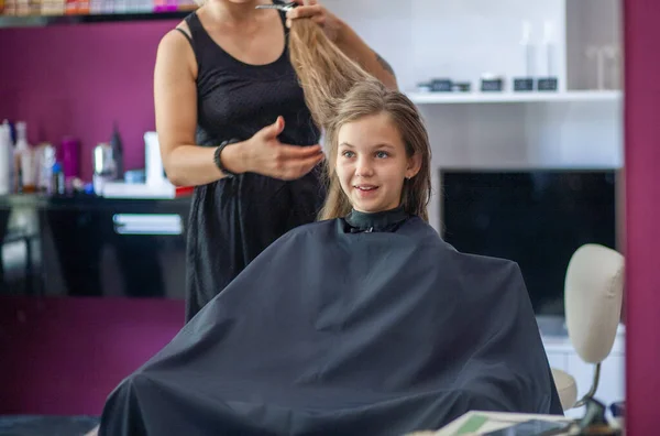 Beautiful young European girl sits in a beauty salon, professional hairdresser stylist works with long hair of a girl.