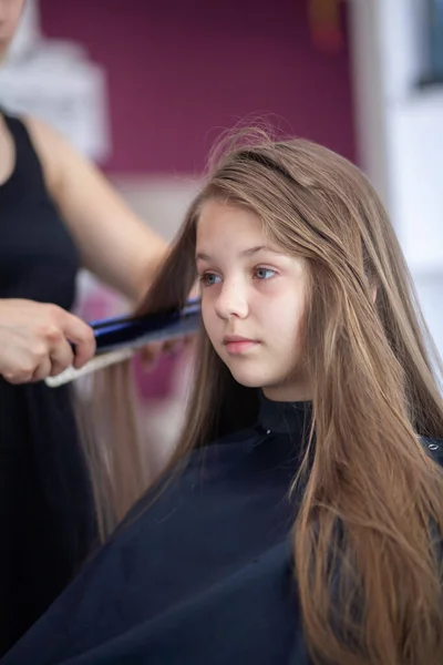 美しい若いヨーロッパの女の子は美容室に座っています 女の子の長い髪を持つプロの美容師の作品 — ストック写真