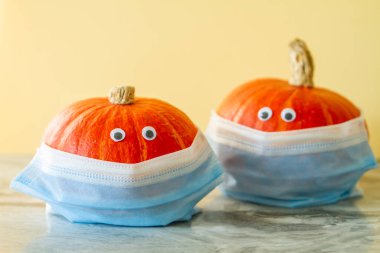 Oyuncak gözlü ve yüz maskesi 95 olan iki parlak turuncu balkabağı. Tatillerde koronavirüs kavramı..