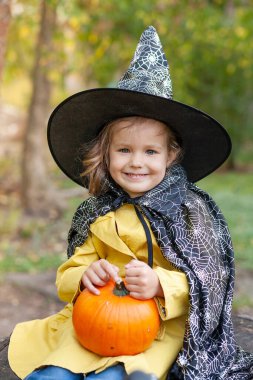 Parkta büyücü şapkası takan küçük bir kız. Bebek elinde bir balkabağı tutuyor. Cadılar Bayramı için bir kostüm..