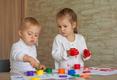 Küçük çocuklar boyayla resim yapar. Çocuklar ellerini gouache ile kirlettiler. Tatlı bir kız ve Down Sendromlu bir erkek yaratıcı olabilir..