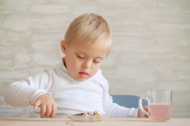 Down sendromu olan küçük bir çocuk evde bir masada oturuyor..