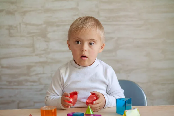 Little cute boys with a genetic disease are sitting at the table. child with Down Syndrome plays with 3D geometric figures. Plastic in toys.