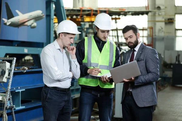 Portrait of a 3 men in a airplane manufactory. Two company managers and one factory worker deciding future plans. Business solution.