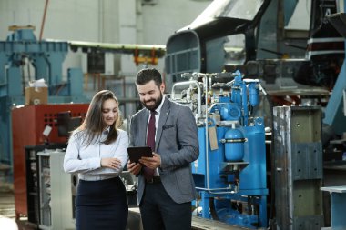 Sağlam bir iş adamının portresi elinde dizüstü bilgisayarı ve tabletiyle fabrika mali raporundan bahsediyor. Sanayi işçileri.