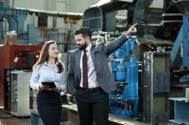 Sağlam bir iş adamının portresi elinde dizüstü bilgisayarı ve tabletiyle fabrika mali raporundan bahsediyor. Sanayi işçileri.