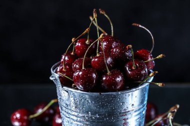 Siyah arka planda metal kovada kırmızı kirazlar. Yaz tadı. Taze böğürtlen suyun altında