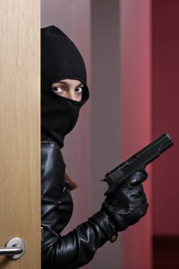 Siyah ceketli ve siyah maskeli bir kadının elinde siyah bir silah olan bir ev soygunu. Maskeli bir hırsız. Maskeli bir hırsız başkalarının evine girmeye çalışıyor.