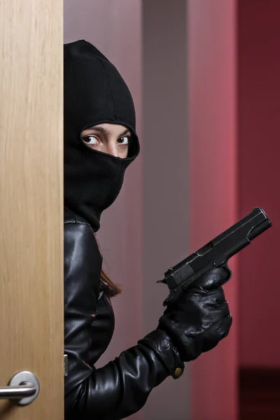 House robbery by woman in a black jacket and black mask holding black gun. Burglar in a mask. Thief in a mask trying to break into other people\'s apartments