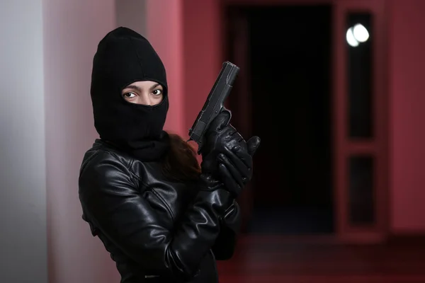 House robbery by woman in a black jacket and black mask holding black gun. Burglar in a mask. Thief in a mask trying to break into other people\'s apartments