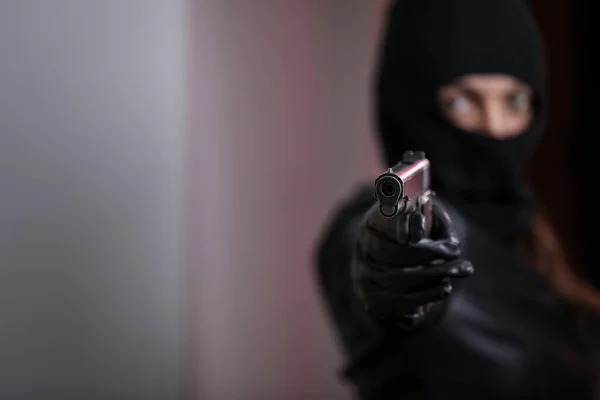Thief broke into the apartment. House robbery by woman in a black jacket and black mask holding black gun. Burglar in a mask. Thief in a mask trying to break into other people\'s house