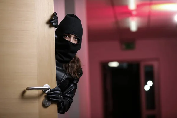 Thief broke into the apartment. House robbery by woman in a black jacket and black mask. Burglar in a mask. Thief in a mask trying to break into other people\'s house