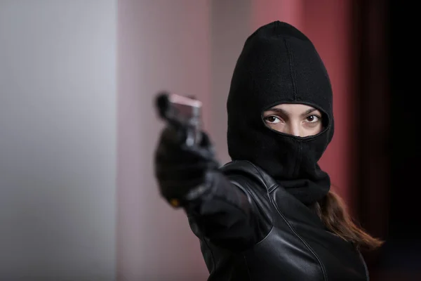 House robbery by woman in a black jacket and black mask holding black gun. Burglar in a mask. Thief in a mask trying to break into other people\'s apartments