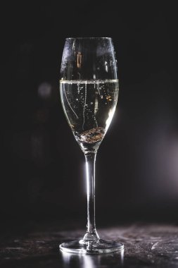 İki altın yüzük siyah arka planda bir kadeh şampanyaya düşer. Gelin ve damat alyansları. 