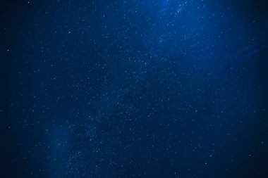 Kırsalda yıldızlı, gece mavisi gökyüzünün yatay görüntüsü. Samanyolu bulutların altında.