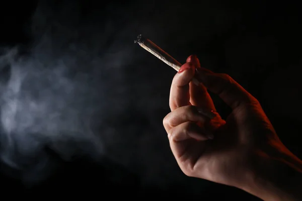 stock image Woman hand holding cigarette in a smoke against black background. Smoking cannabis joint. Medical use. 