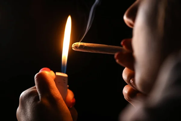 黒い背景の煙の中でタバコを持っている女性の手 大麻の共同喫煙 医療用 — ストック写真
