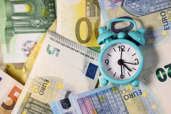 Avro banknotlarının arka planında küçük mavi alarm saati. Mali işler. Finansal kriz. Bankacılık sistemi. Ekonomik bir sorun. Enflasyon. Para yazdırma.