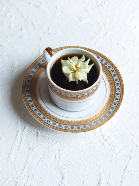 The flower in the cup. A little white rose in a cup of black coffee. The concept of comfort and beauty.