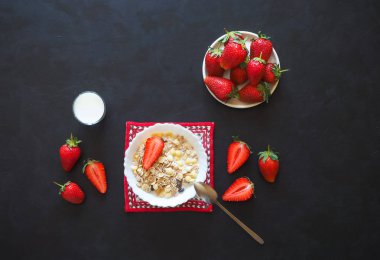 Çilek kahvaltı. Müsli, süt ve siyah masada olgun çilek.