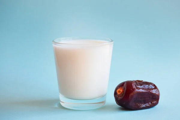 Um copo de leite e uma data madura num fundo azul. Comida Ramadã . — Fotografia de Stock