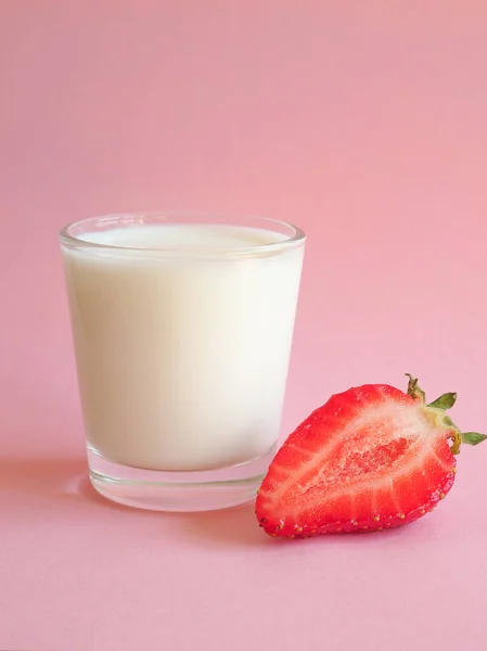 Ett glas mjölk och en mogen jordgubbe på en rosa bakgrund. — Stockfoto