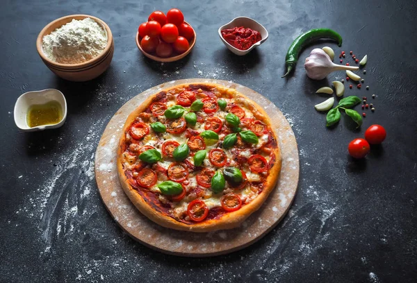 Italian pizza Margarita with cherry tomatoes and green basil on black background.