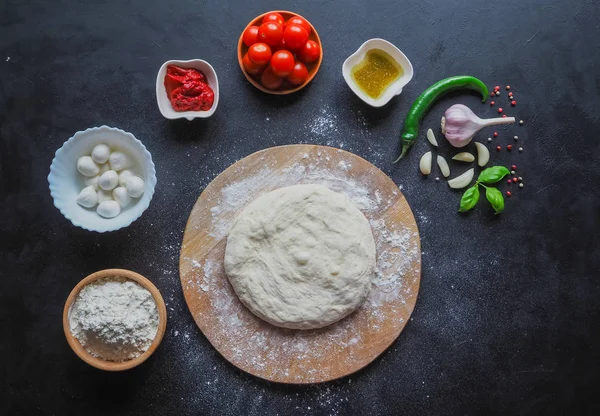 Deg och en uppsättning pizza ingredienser på ett svart bord. Produktion av italiensk pizza Margarita. Skede av produktionen. — Stockfoto