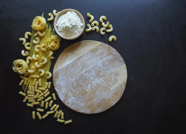 Espaguetis de pasta italiana, tagliatelle, fusilli, cavatappi sobre fondo negro. Pasta en forma de media luna . — Foto de Stock