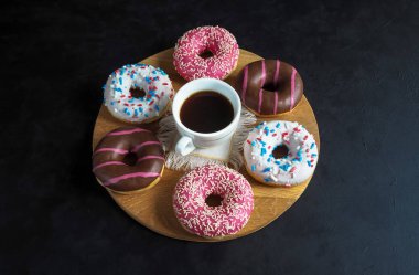 Bir fincan kahve ve çörek tatlılar siyah bir tablo.