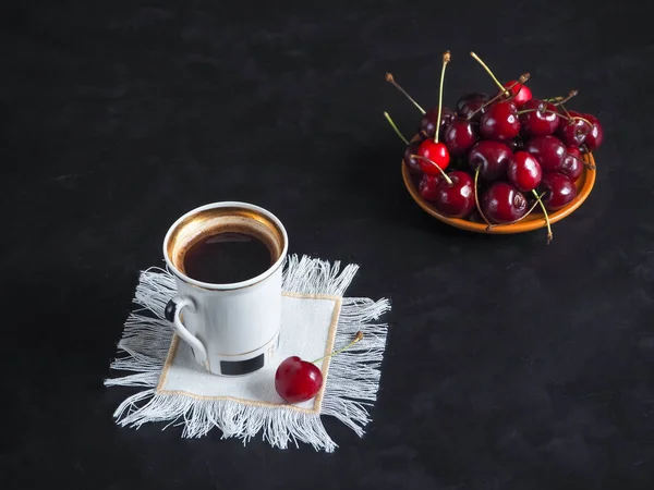 Een kopje koffie en zoete kersen op een zwarte lijst. — Stockfoto