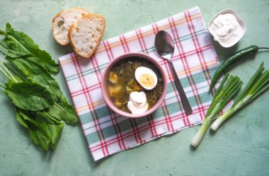 Yeşil çorba bir kase. Kuzukulağı çorbası ile yumurta ve yaprakları, soğan, yeşil bir masada ekmek. 